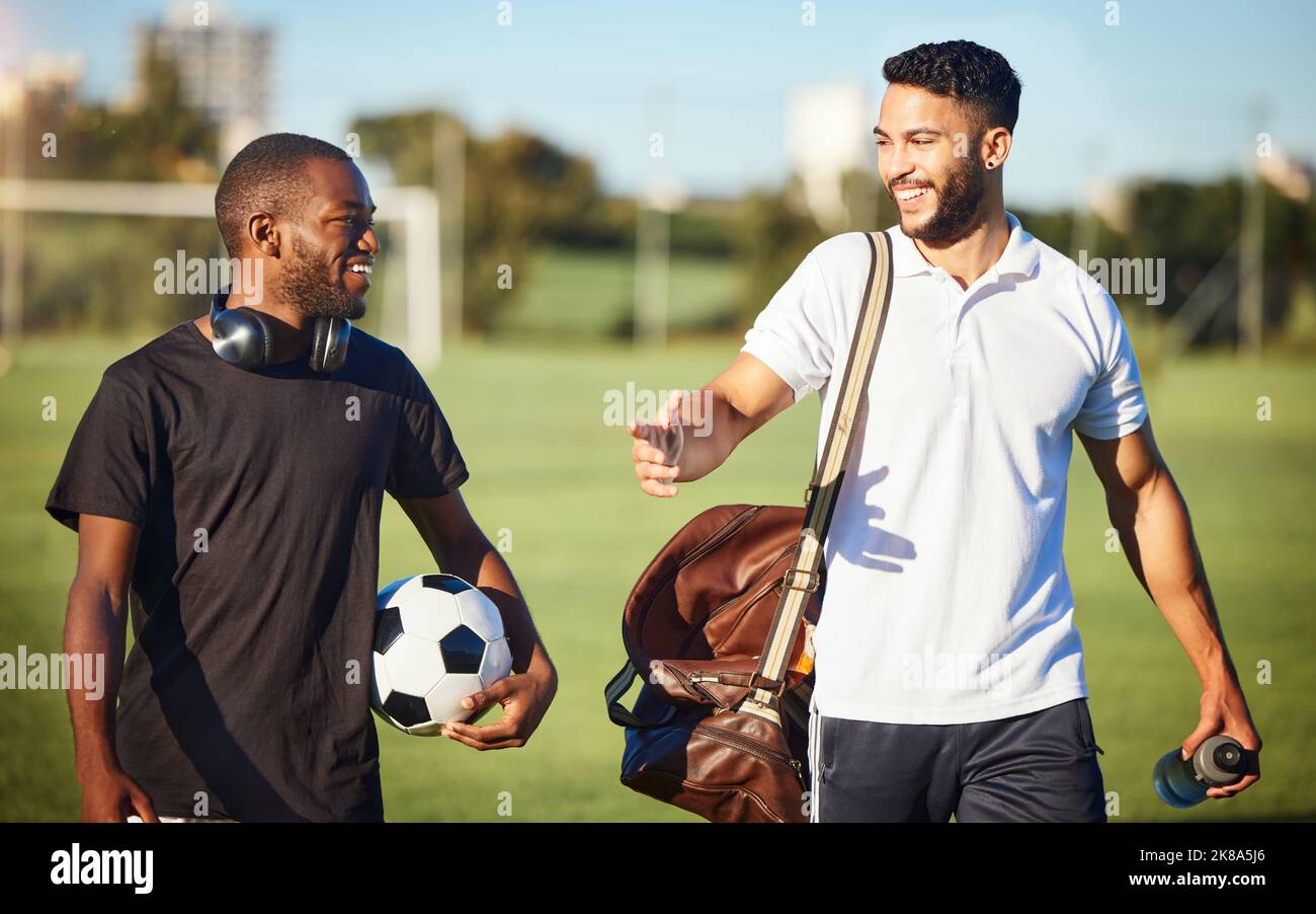 Fußballspieler, Freunde und Männer, die nach dem Training oder dem Fitnesstraining auf dem Rasen auf dem Fußballfeld spazieren gehen. Vielfalt, Lächeln und Fußballspieler Stockfoto