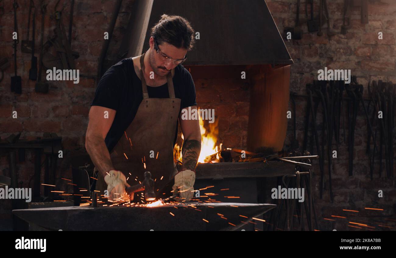 Metall kann alles und alles sein, was Sie wollen. Ein Metallarbeiter trifft in einer Schweißwerkstatt mit einem Hammer auf einen heißen Metallstab. Stockfoto