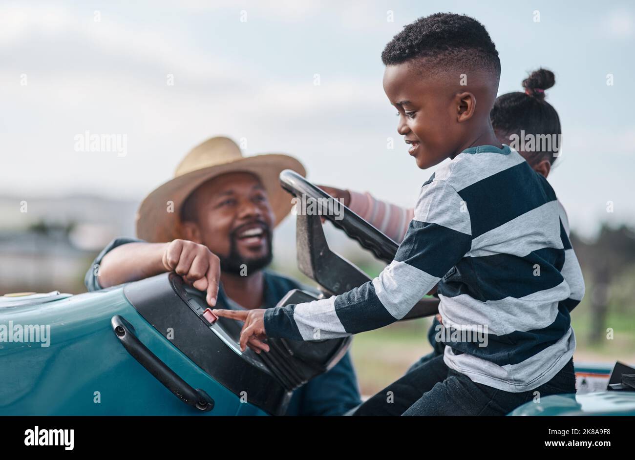 Jeder Junge erinnert sich an seine erste Traktorfahrt. Ein reifer Mann, der seinem entzückenden Sohn und seiner Tochter hilft, einen Traktor auf einer Farm zu fahren. Stockfoto