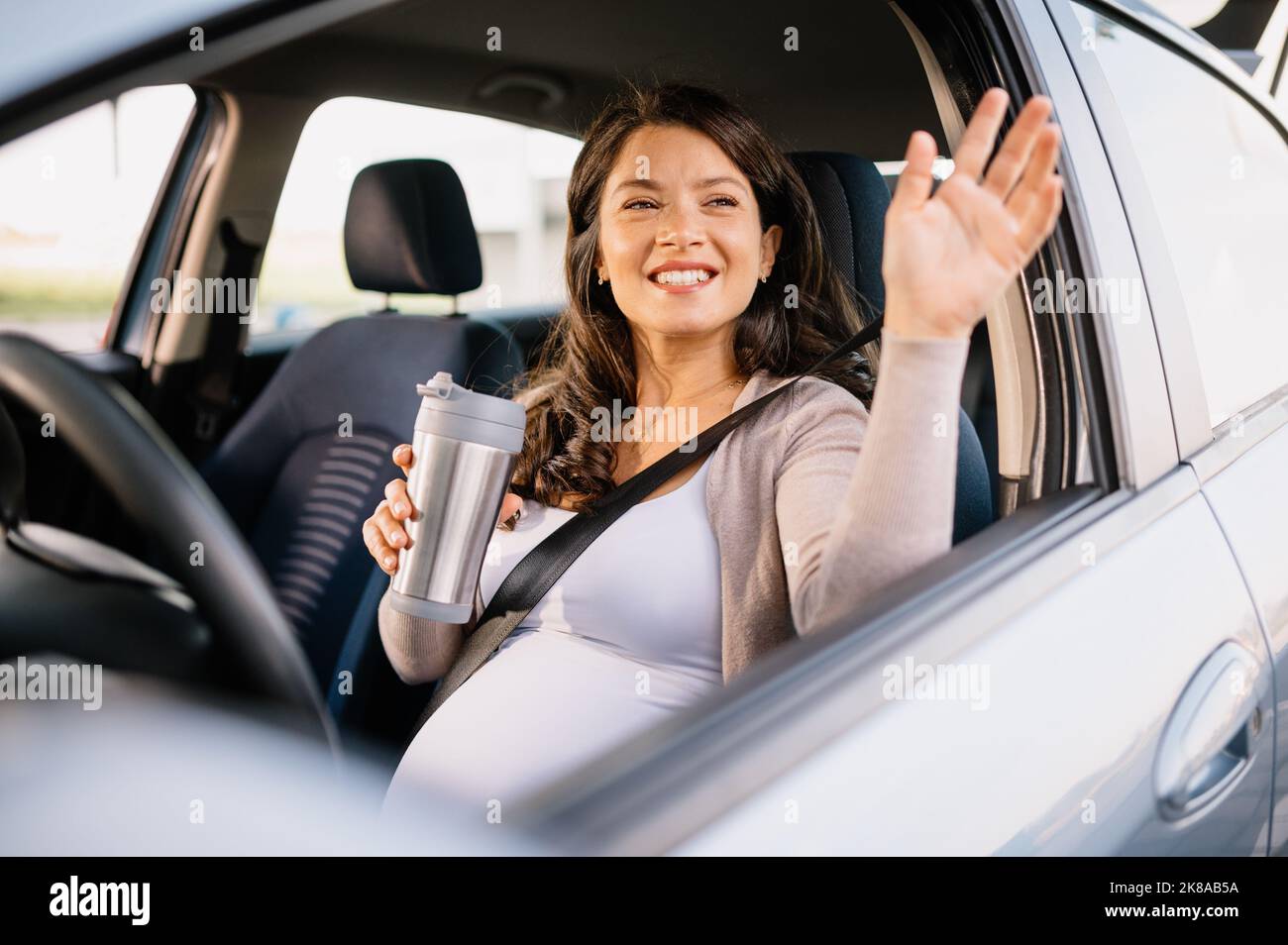 Schwanger kaukasische Frau mit glücklichen Gesicht im Auto sitzen und winken mit der Hand Stockfoto