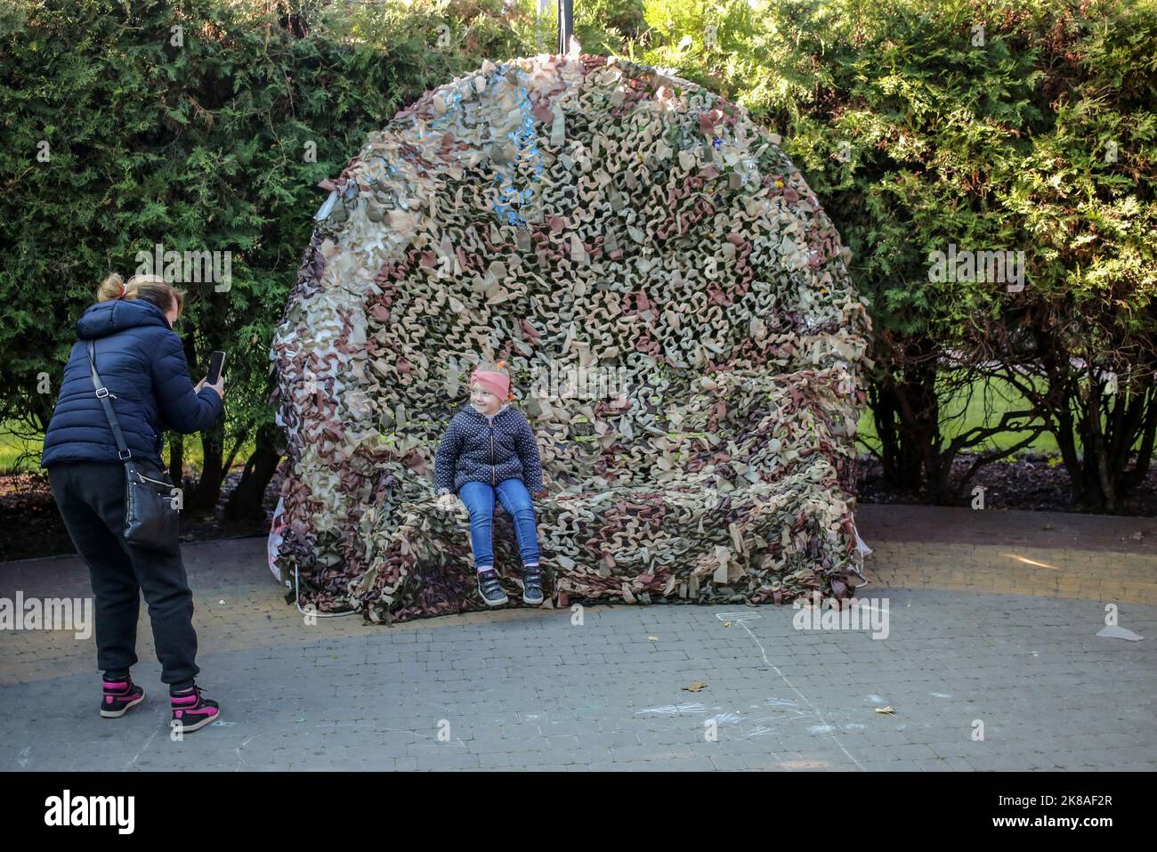 Eine Mutter sah, wie sie ihr Kind fotografierte, das auf einem Tarnnetz für die Bedürfnisse der ukrainischen Streitkräfte sitzt. Tag frei im Park, der nach Maxim Gorky benannt ist. Kinder konnten Bilder aufhängen, die der Ukraine und den Streitkräften der Ukraine gewidmet waren, und lernen, wie man Tarnnetze für die Bedürfnisse der Streitkräfte der Ukraine zusammen mit Erwachsenen webt. Stockfoto