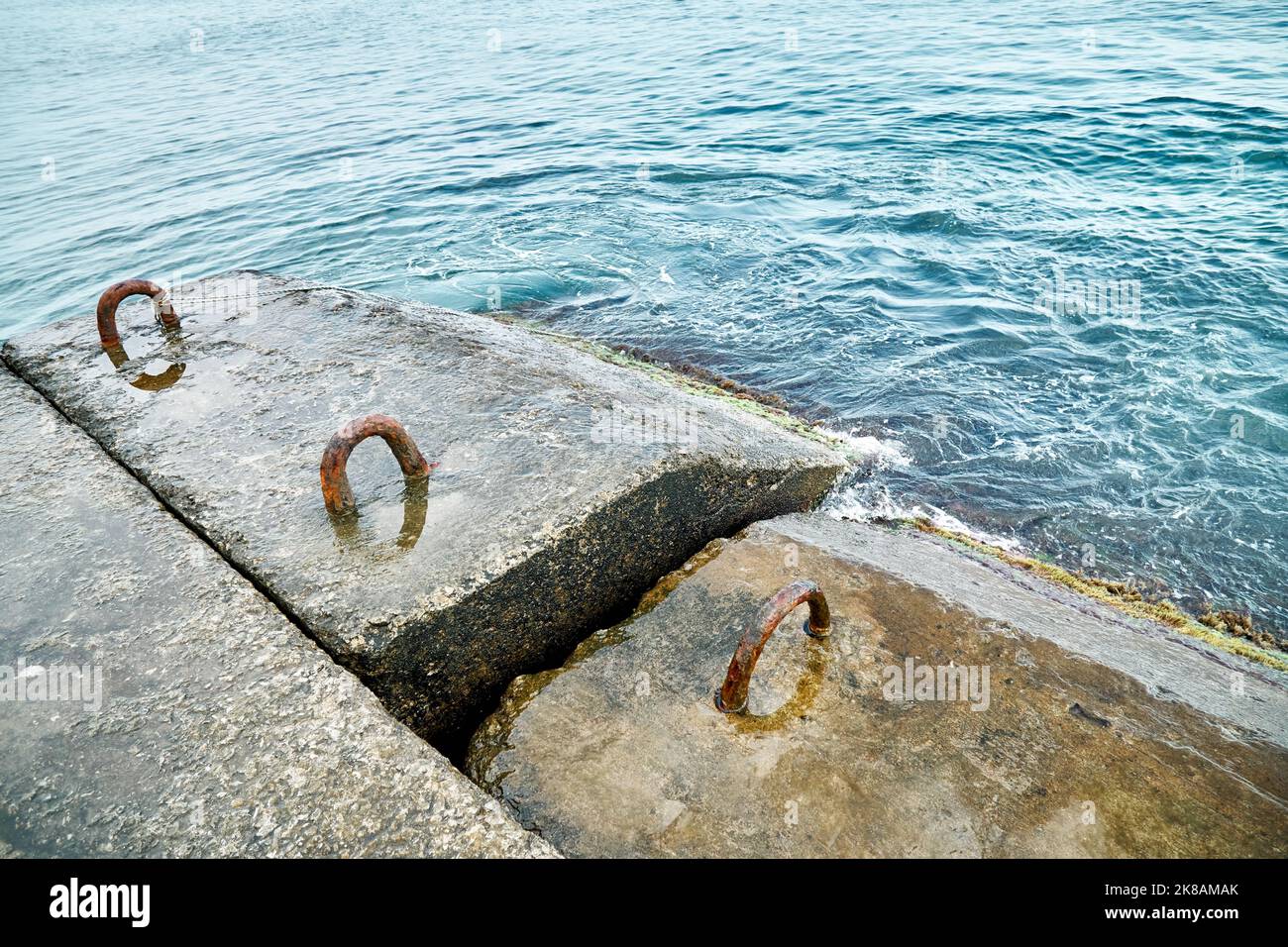 Altes Stahlbeton-Wellenbrechwasser mit Metallschlaufen und Seil im brodelnden Meer Stockfoto