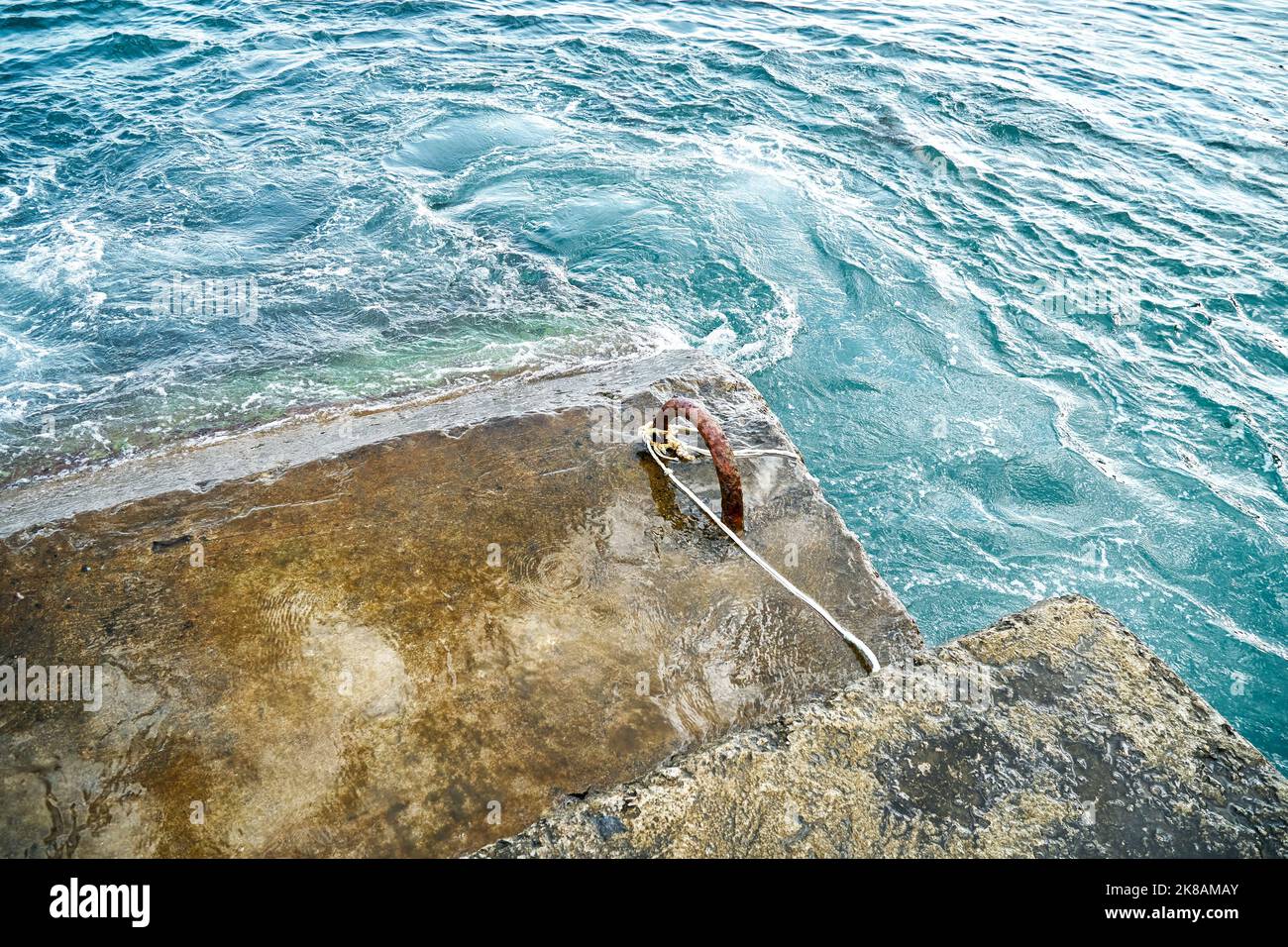 Altes Stahlbeton-Wellenbrechwasser mit Metallschlaufen und Seil im brodelnden Meer Stockfoto