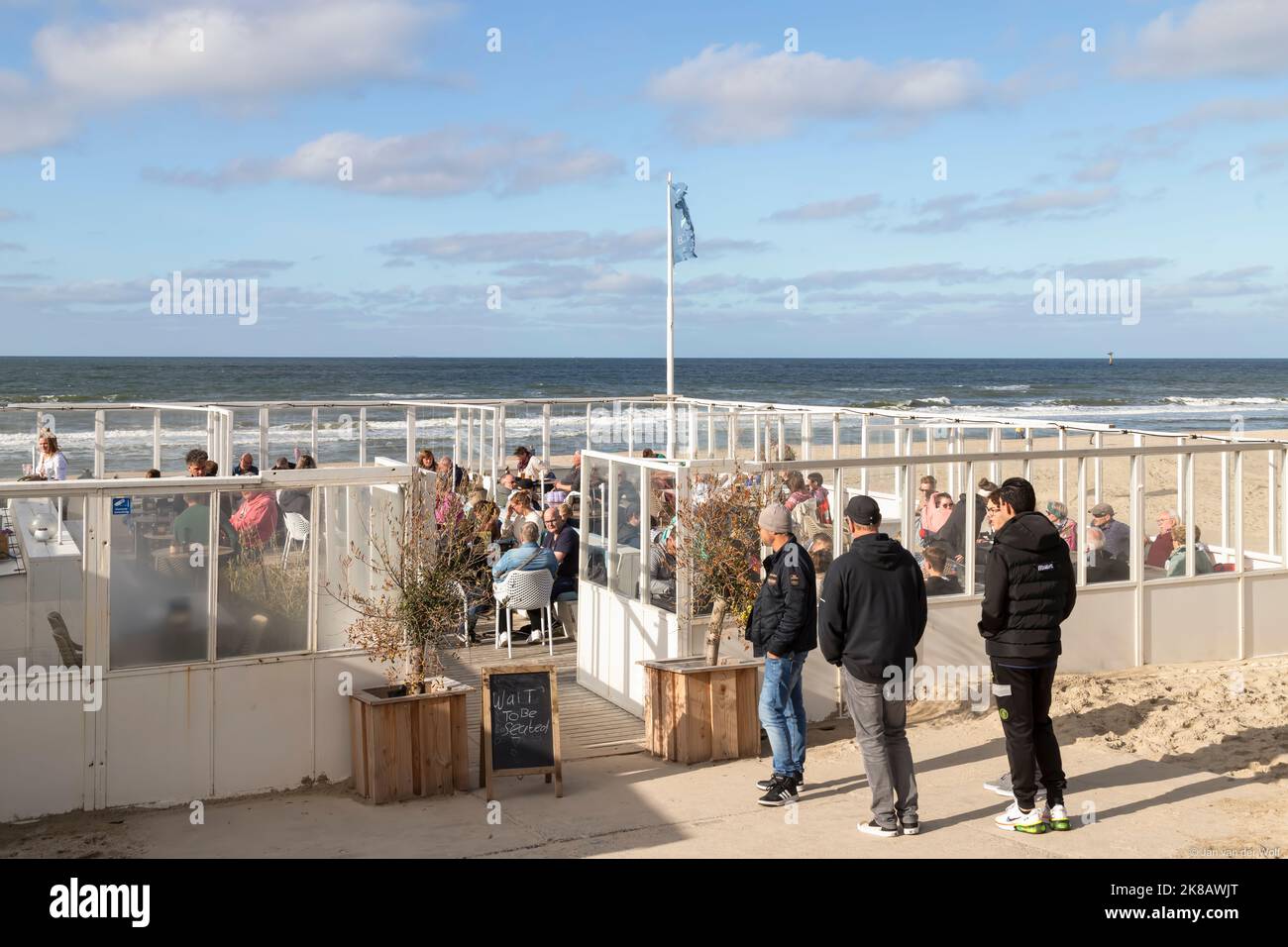 Touristen genießen die Terrasse des Strandpavillons am Strand in der Nähe der Küstenstadt De Koog auf der Insel Wadden in Texel. Stockfoto