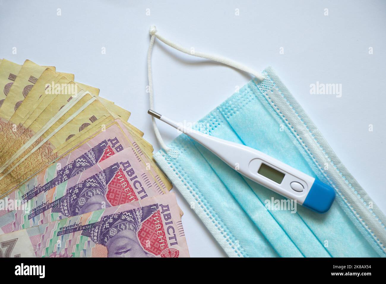 ukrainische Griwna elektronisches Thermometer und medizinische Maske auf weißem Hintergrund, Finanzen und Medizin, Geld und Gesundheit Stockfoto