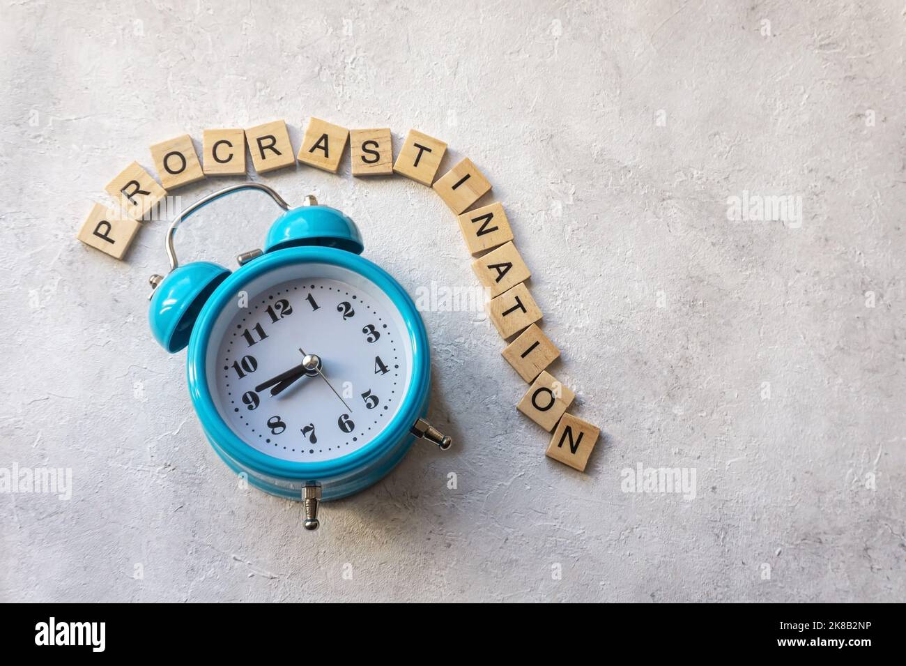Procrastination Text mit blauem Wecker auf betontem Hintergrund. Zeitmanagement-Konzept. Stockfoto