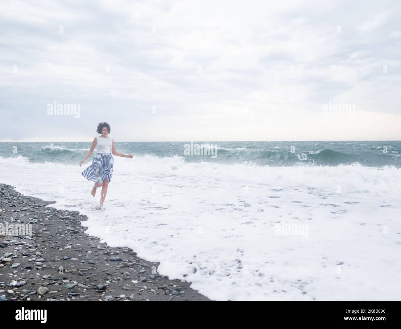 Glückliche Frau läuft auf der Brandung des stürmischen Meeres. Frau mit Haaren zerzauste vom Wind. Fernweh-Konzept. Urlaub an der Küste. Stockfoto
