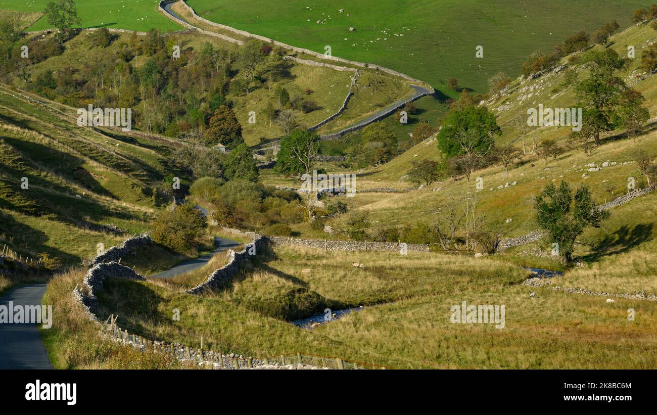 Ruhige, gewellte Landstraße (Talseiten, malerische sonnenbeschienenen Landschaften, steiler Aufstieg, Bach) - in der Nähe von Kettlewell, Yorkshire Dales, England, Großbritannien. Stockfoto