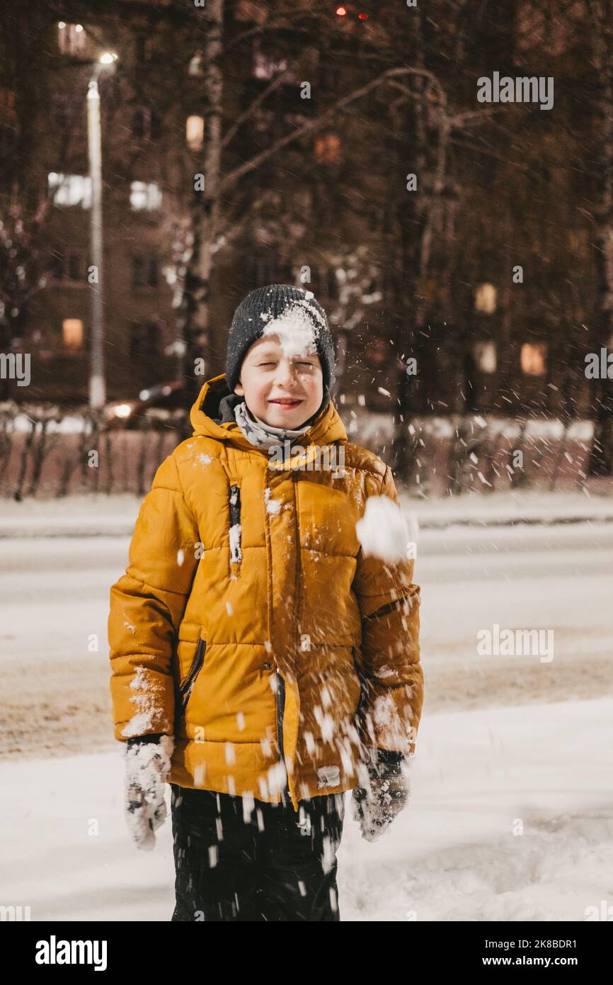 Ein Junge in einer gelben Jacke spielt bei einem Schneefall mit Schnee Stockfoto