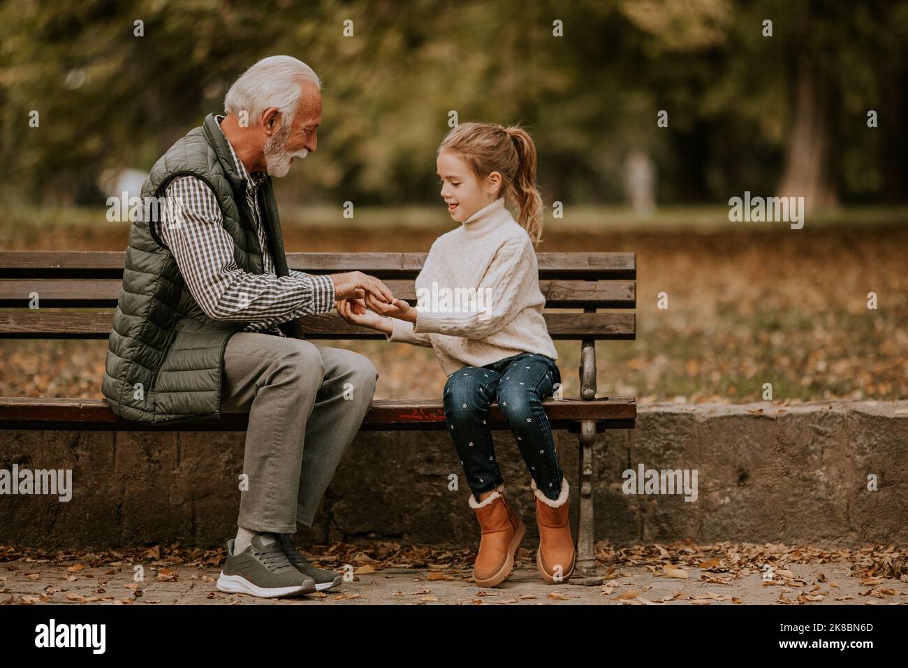 Der gutaussehende Großvater spielt am Herbsttag im Park mit seiner Enkelin ein Spiel mit roten Händen Stockfoto