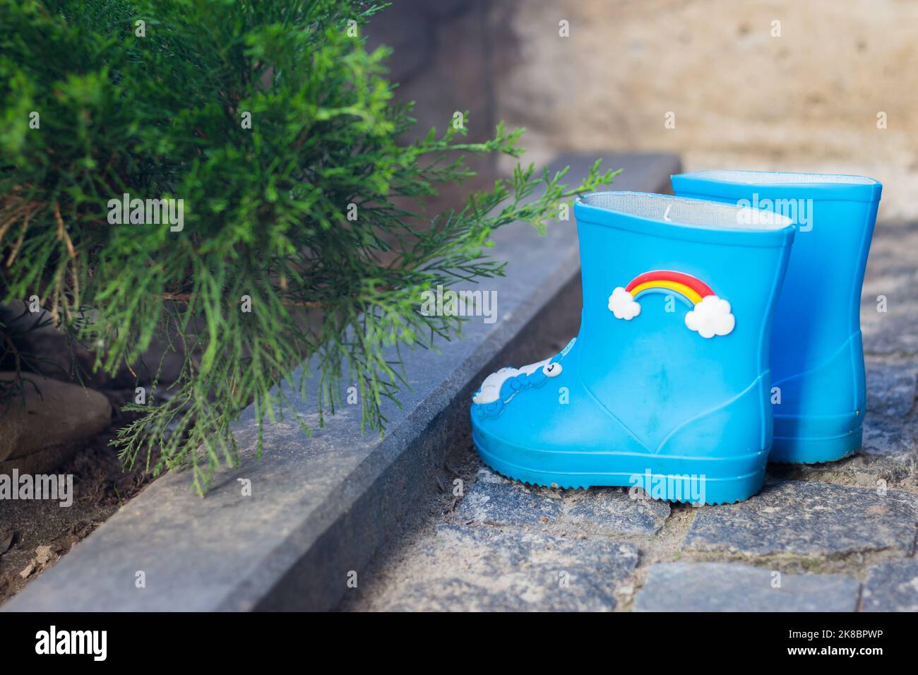 Kinder Gummistiefel im Garten. Niedliche blaue Regenstiefel mit Regenbogendeko. Herbstschuhe. Stiefel für raine Wetter. Kinderschutzkleidung. Stockfoto