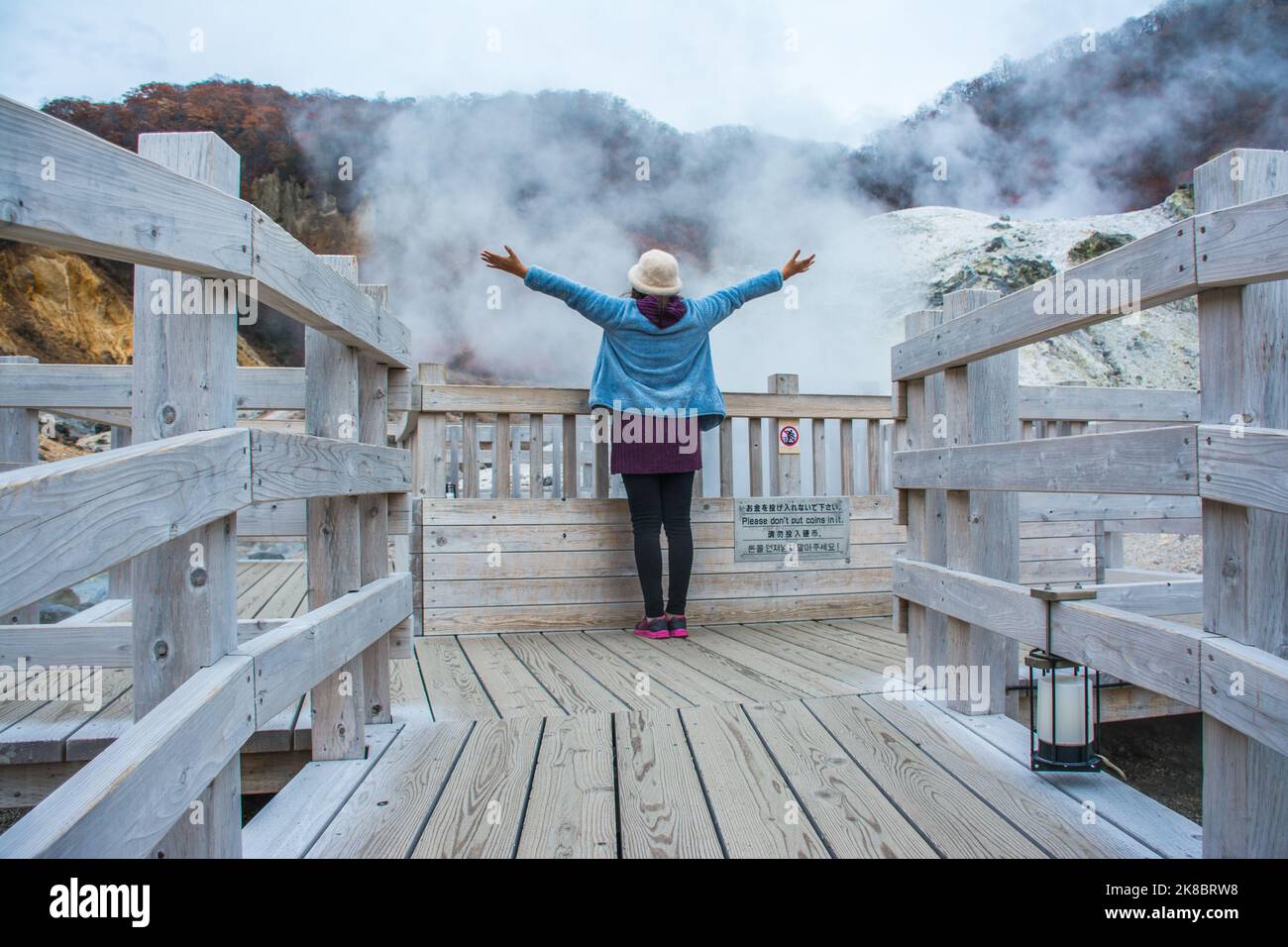 Frau, die in Jigokudani oder im Hell Valley in der Stadt Noboribetsu Onsen steht, heiße Dampfquellen, schwefelhaltige Bäche und andere vulkanische Aktivitäten, heiße Spri Stockfoto