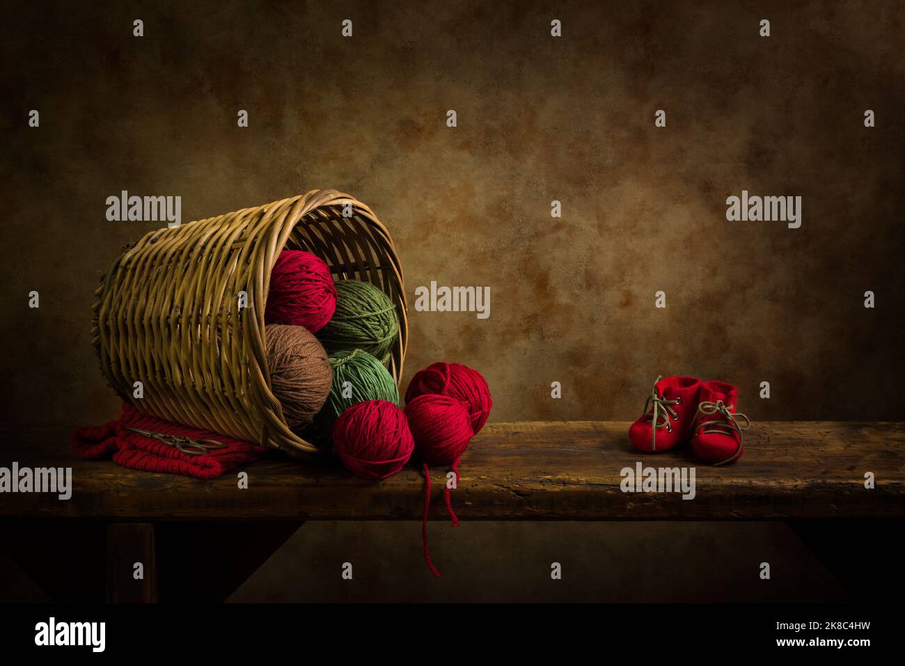 Alter Korbkorb mit roten und grünen Wollkugeln auf einem rustikalen alten Holzregal. Dies ist für digitales Compositing geeignet. Stockfoto
