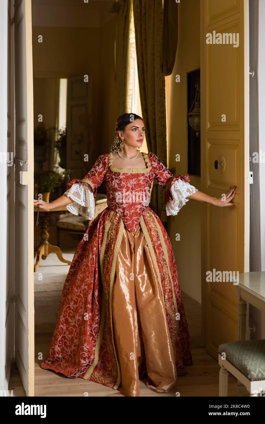 Schöne Frau in Spätrenaissance-Kostümen, die zwischen den offenen Türen eines mittelalterlichen Schlosses posiert. Stockfoto