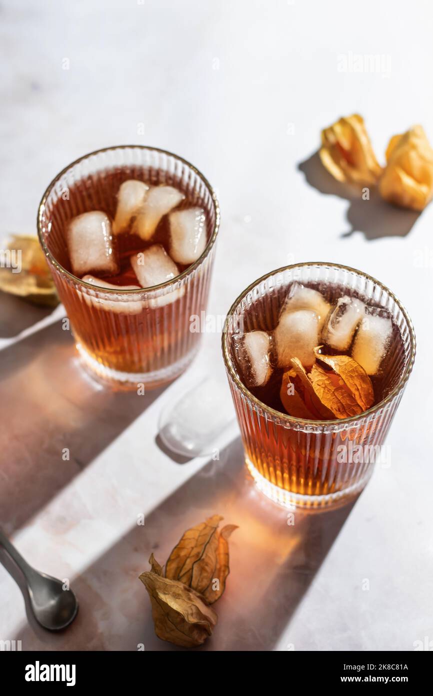 Orange gesunde kalte Getränke-Cocktails mit Physalis-Beere auf Marmorboden. Trinken Foto mit hartem Licht und klaren Schatten. Herbstparty Stockfoto