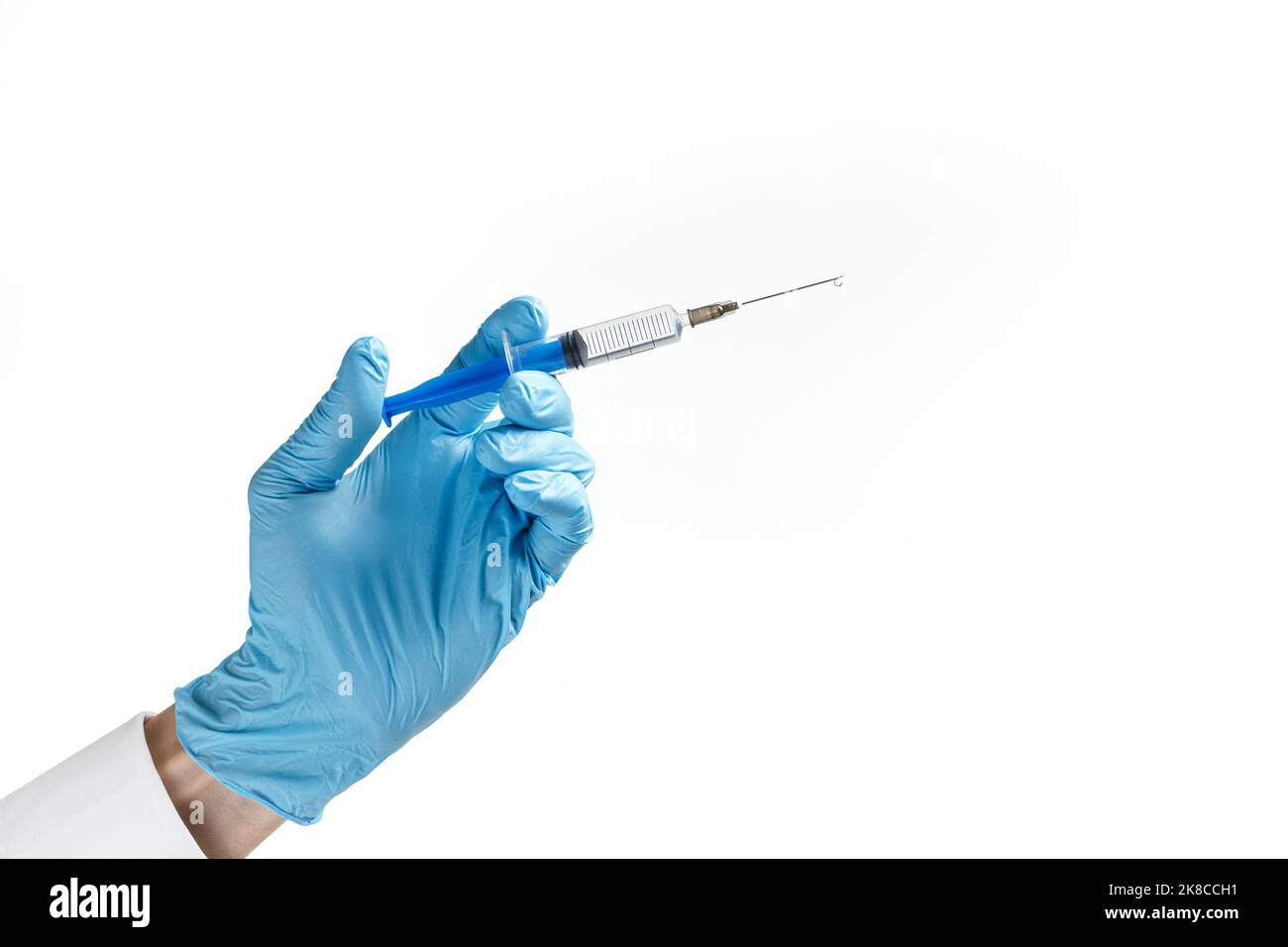 Spritze mit einem Tropfen auf einer Nadel in der Hand in einem blauen Gummihandschuh auf weißem Hintergrund. Medizinisches Injektionskonzept. Stockfoto