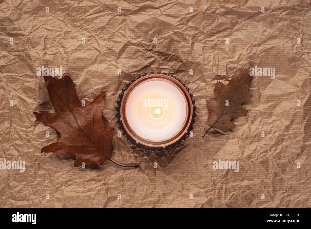 Duftkerze und braune Herbstblätter auf zerknittertem Papierhintergrund. Herbstkonzept. Draufsicht, flach liegend Stockfoto