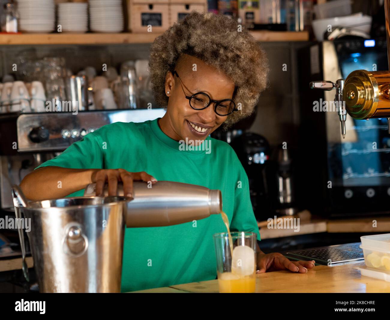 Glückliche afroamerikanische Kellnerin, die einen Cocktail oder Drink in einem Pub serviert. Stockfoto