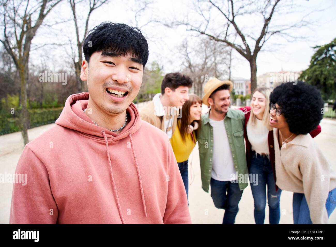 Junger lächelnder asiatischer Kerl, der mit einer Gruppe von Freunden die Kamera im Freien anschaut. Glückliche Menschen gemeinsam Spaß haben Konzentrieren Sie sich auf einen jungen Chinesen Stockfoto