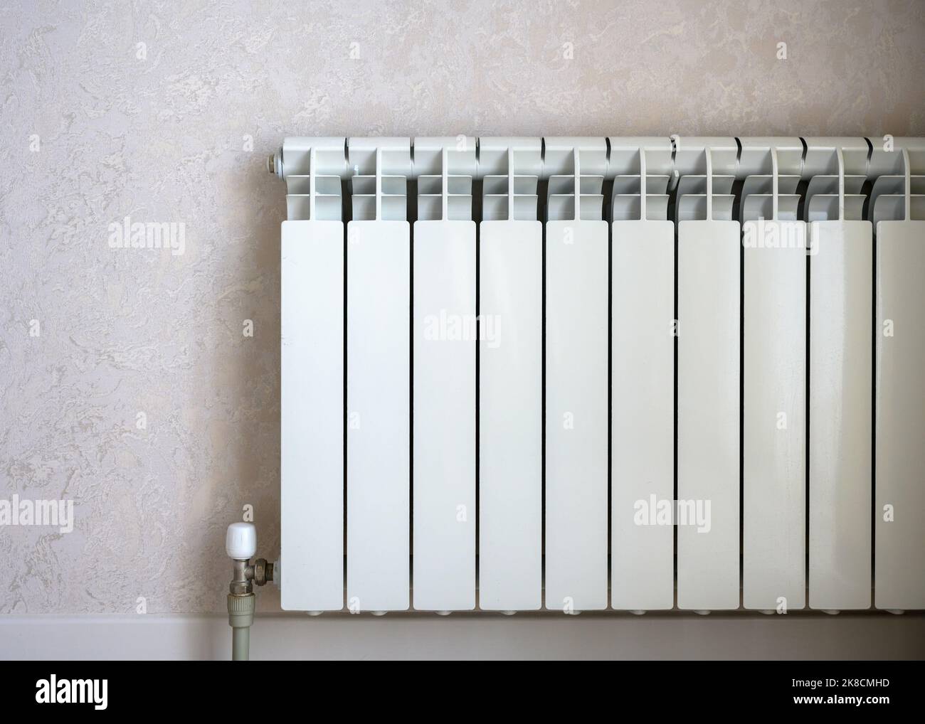 Heizkörper auf hellem Wandhintergrund, weißer Metall-Wasserkocher im Wohnzimmer. Konzept von Wärme, Energiekrise, Einsparung, moderne Heizkörper. Stockfoto