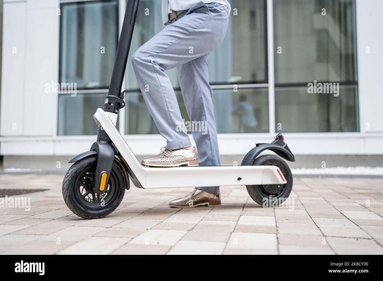 Füße von unbekannten Frau stehen oder fahren weißen Elektro-Kick Scooter E-Scooter auf dem Bürgersteig am Tag umweltfreundliche moderne Transport in der Stadt oder Stockfoto