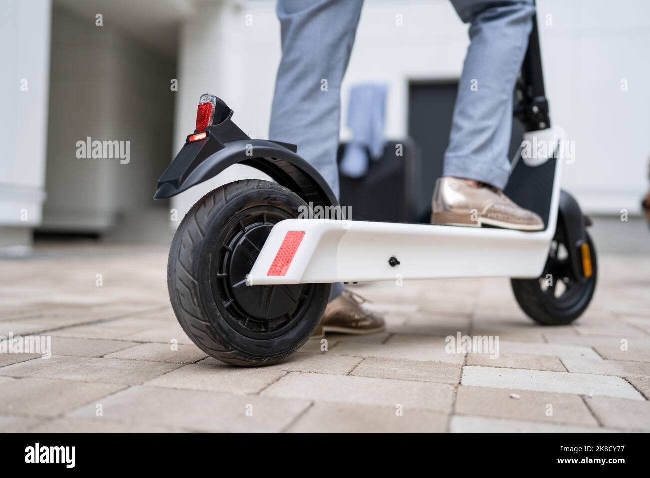 Füße von unbekannten Frau stehen oder fahren weißen Elektro-Kick Scooter E-Scooter auf dem Bürgersteig am Tag umweltfreundliche moderne Transport in der Stadt oder Stockfoto