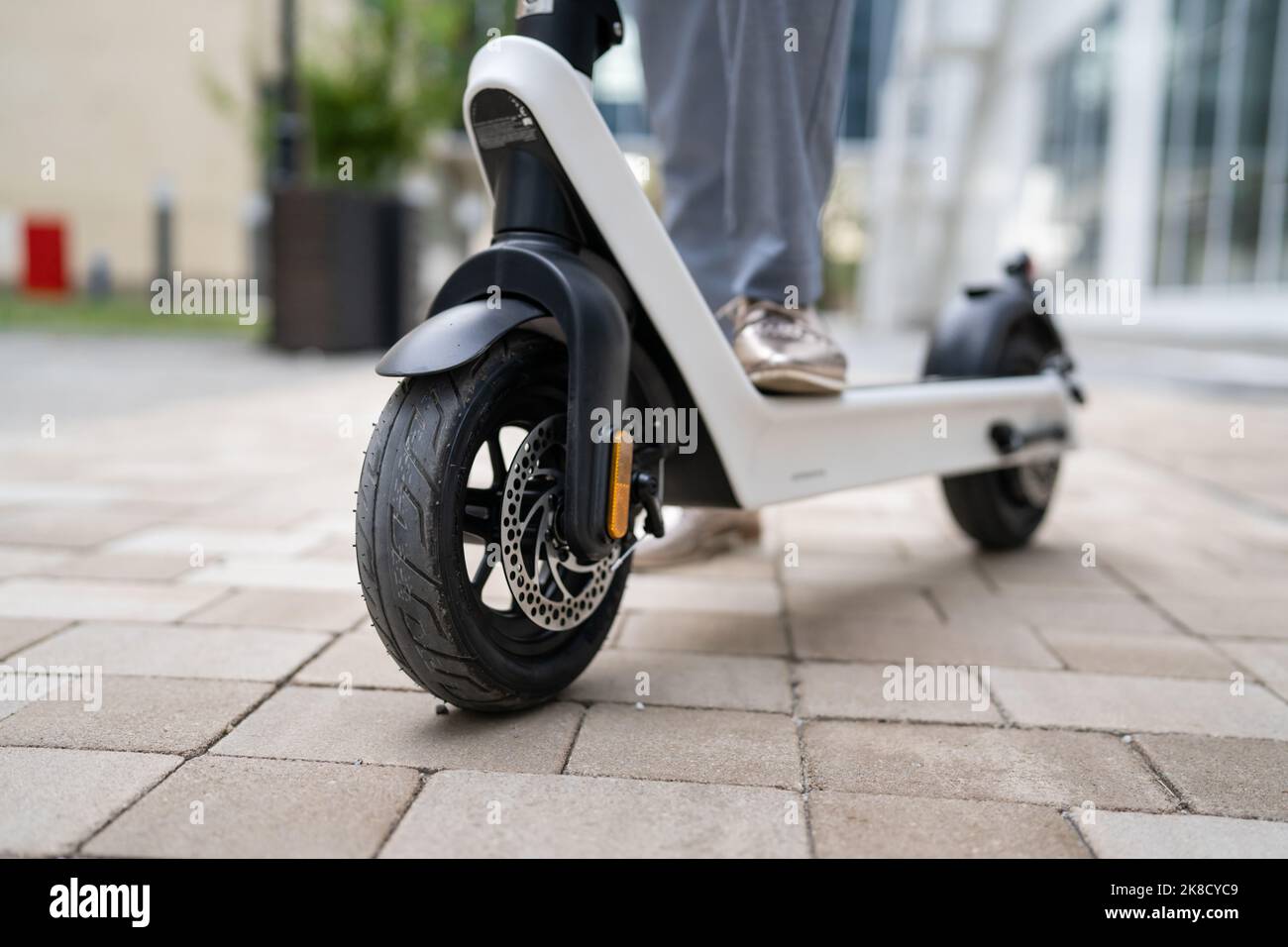 Füße von unbekannten Frau stehen oder fahren weißen Elektro-Kick Scooter E-Scooter auf dem Bürgersteig am Tag umweltfreundliche moderne Transport in der Stadt oder Stockfoto
