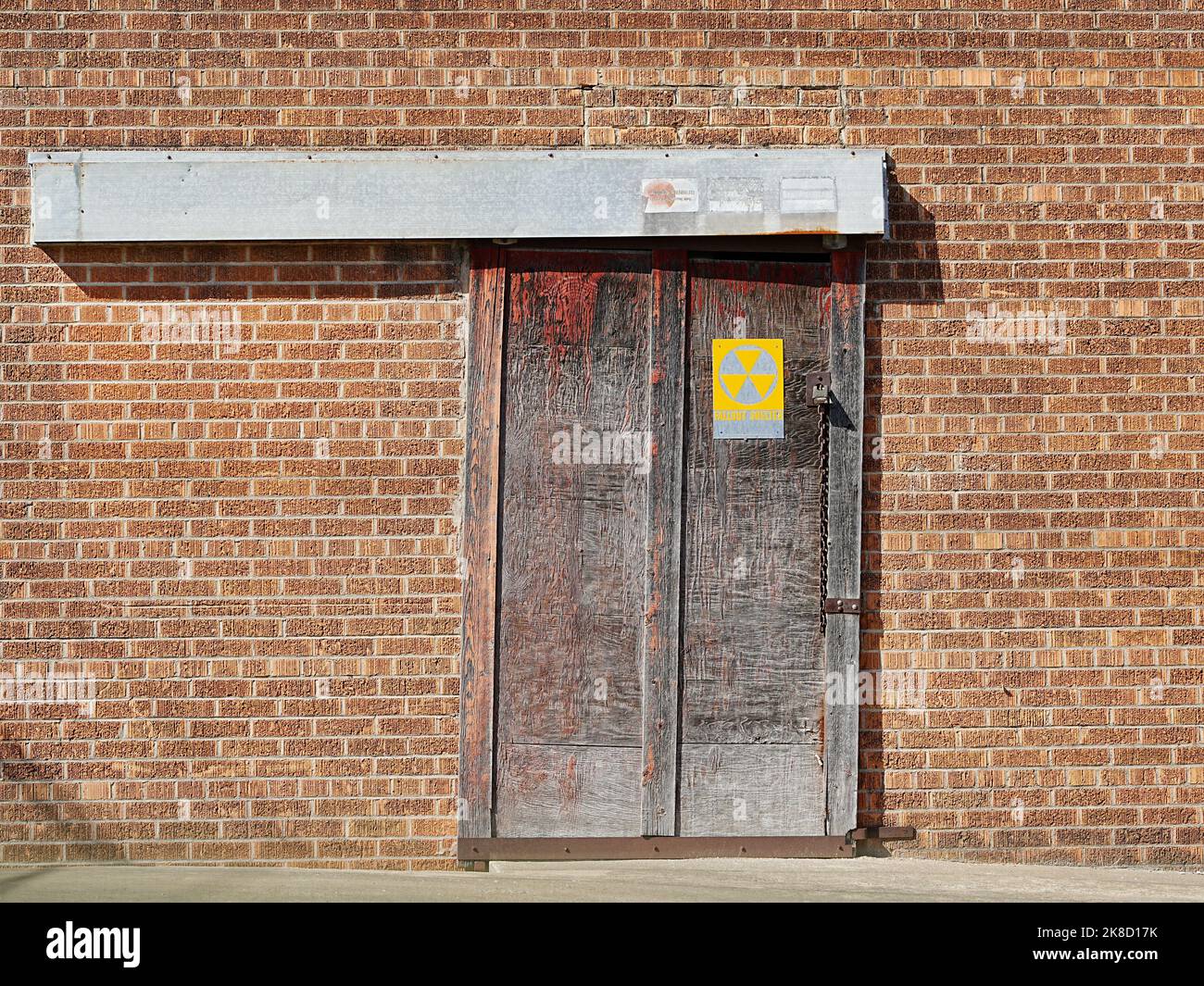 Taylor, Texas, USA – Backsteinwand mit alter Schiebetür und Schild mit radioaktivem Fallout-Schutz Stockfoto