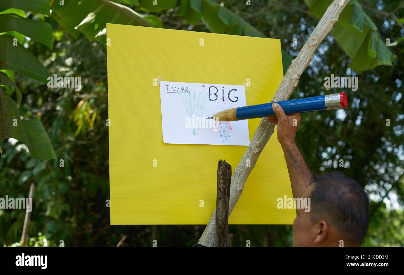Ein Künstler, der in einem tropischen Garten mit einem sehr großen Bleistift zeichnet. Stockfoto