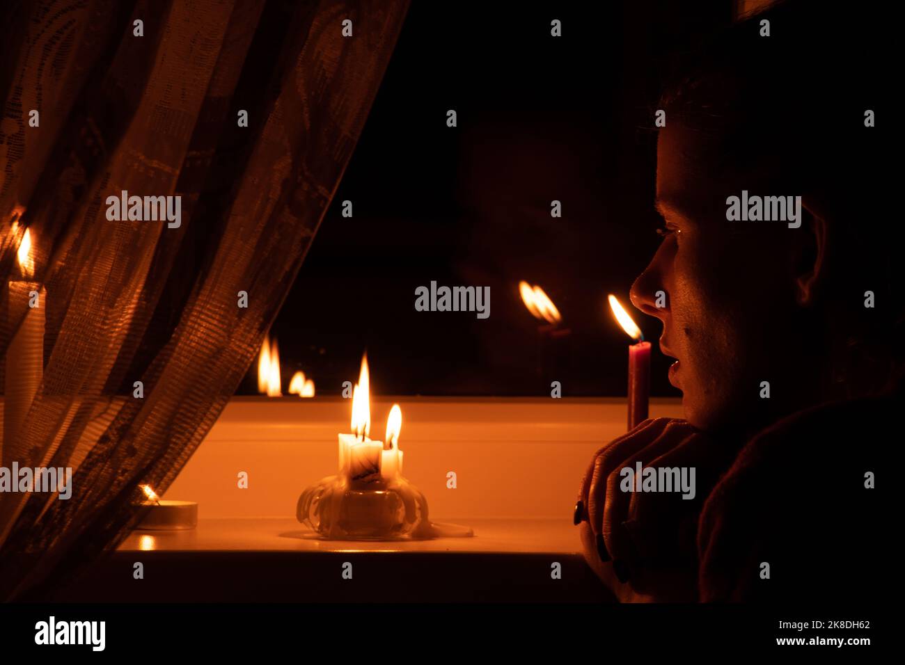 Das Gesicht des Mädchens setzte Kerzen auf das Fenster einer Wohnung in der Ukraine, in der Ukraine, die wegen des Krieges keinen Strom hatte, einer Wohnung ohne Licht Stockfoto Das Gesicht des Mädchens setzte Kerzen auf das Fenster einer Wohnung in der Ukraine, in der Ukraine, die wegen des Krieges keinen Strom hatte, einer Wohnung ohne Licht Stockfoto