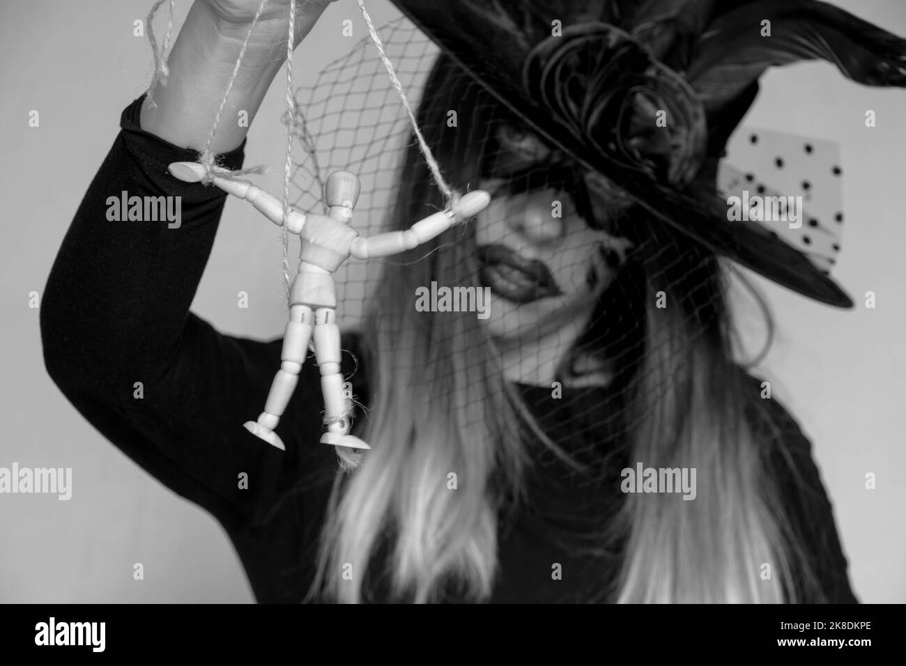 Die Hexe hält eine Holzpuppe eines Mannes an den Seilen, Manipulation von Menschen und Macht, Magie und Tyrannei, willensschwache Menschen Stockfoto
