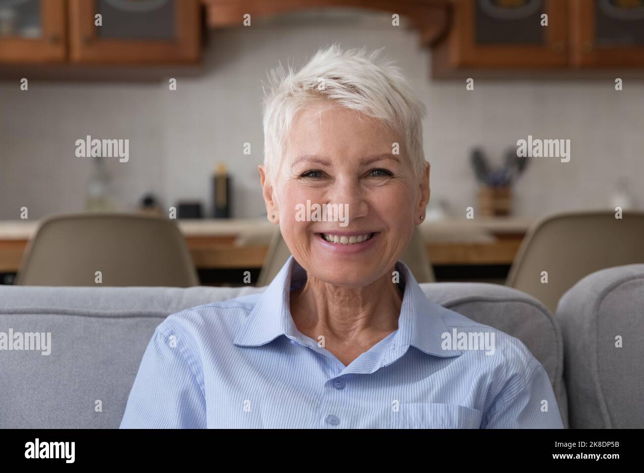Ältere Frau, die sich lächelnd auf dem Sofa ausruht und die Kamera anstarrt Stockfoto