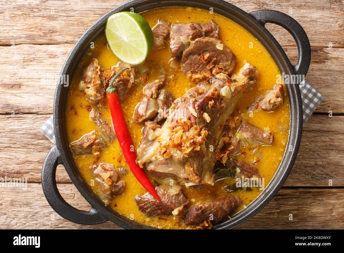Gulai Kambing oder indonesische traditionelle köstliche Ziegencurry in der Pfanne auf dem Holztisch. Horizontale Draufsicht von oben Stockfoto