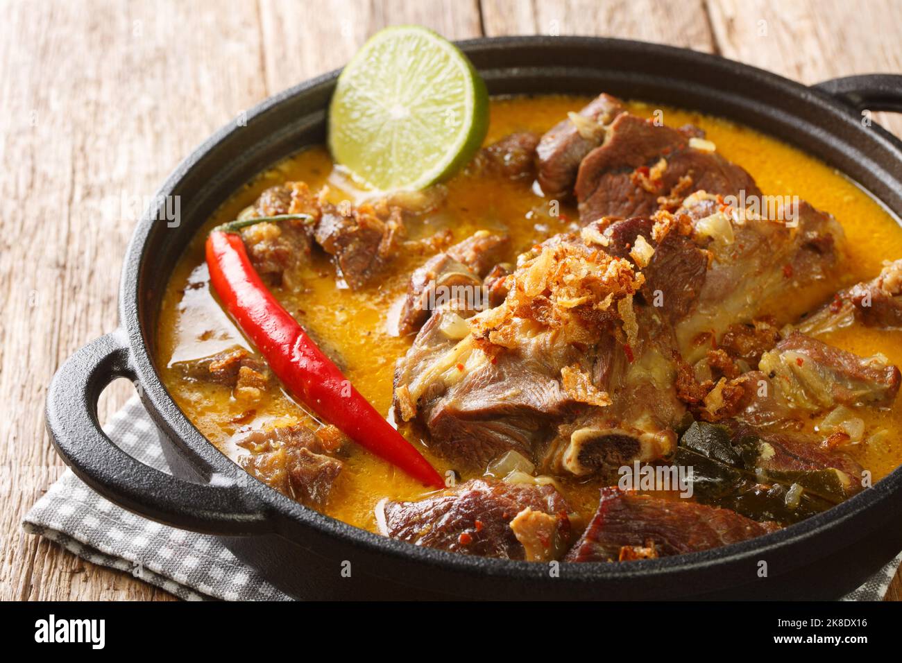 Gulai Kambing oder indonesische traditionelle köstliche Ziegencurry in der Pfanne auf dem Holztisch. Horizontal Stockfoto