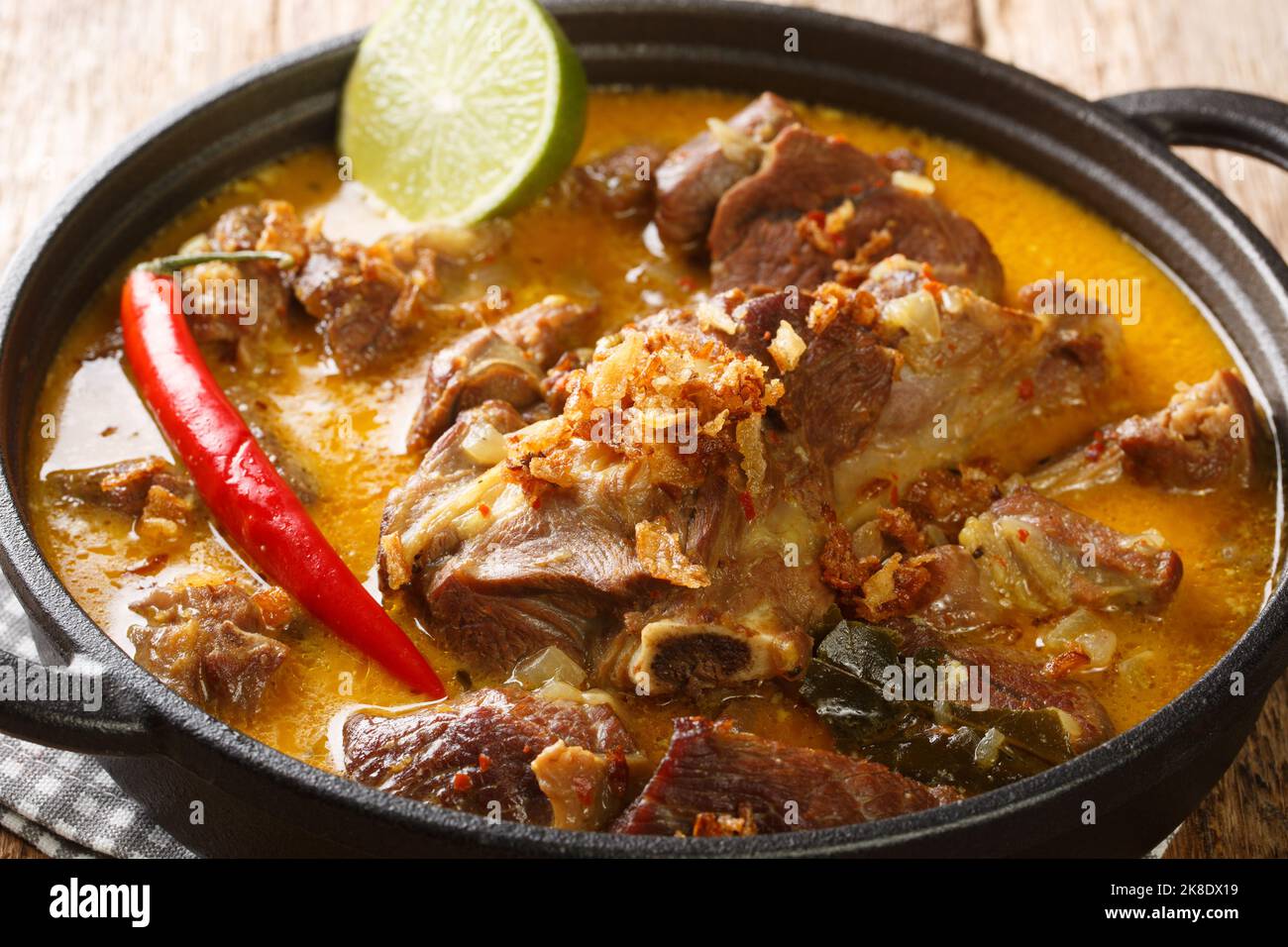 Gulai Kambing traditioneller javanischer Hammelfleisch-Eintopf aus der Nähe auf der Pfanne auf dem Holztisch. Horizontal Stockfoto