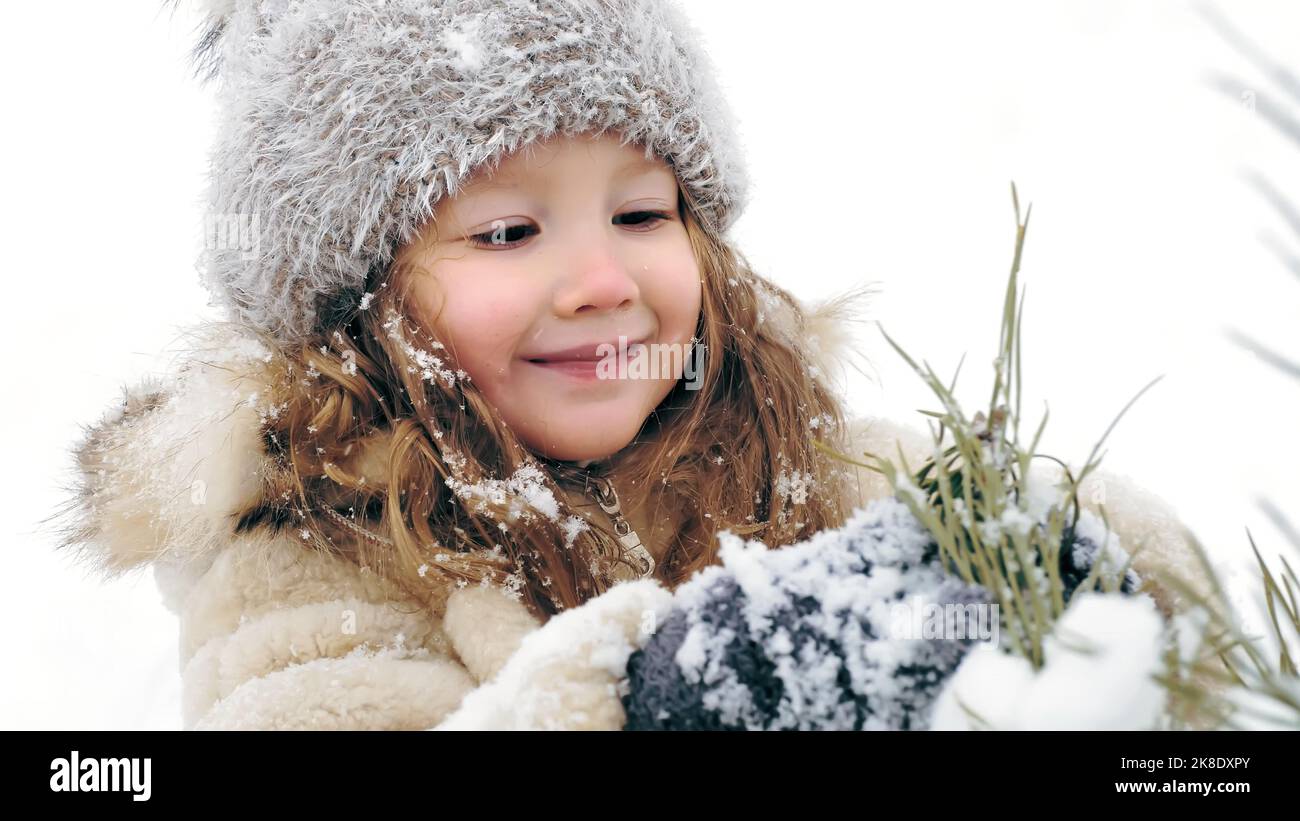 Weihnachtsbaum Outdoor-Dekoration. Cutie, hübsches kleines Mädchen schmückt schneebedeckten Weihnachtsbaum mit hausgemachten Eisspielzeug, während Schneefall, im Wald. Glückliche Zeit am verschneiten Wintertag. Winter Familienaktivität im Freien. Zeitlupe. Hochwertige Fotos Stockfoto