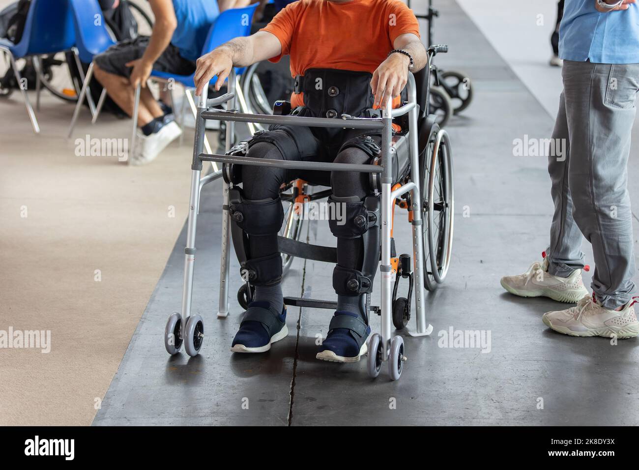 Junge mit Bewegungsproblemen in den unteren Gliedmaßen sitzt in einem Rollstuhl bereit, aufrecht zu stehen dank eines mechanischen Exoskeletts. Stockfoto