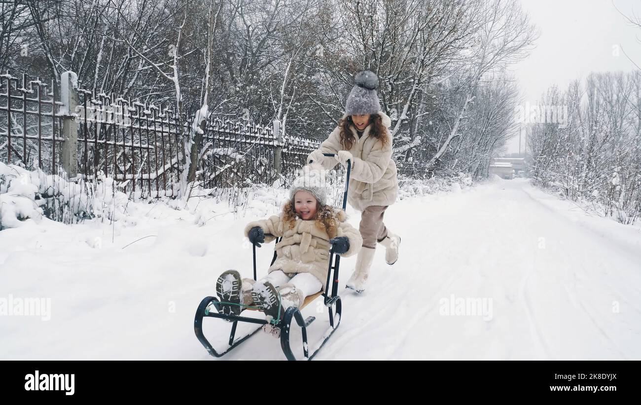 Familienrodeln im Winter. Outdoor Winteraktivitäten. Fröhliche, lachende, verspielte Kinder genießen das Rodeln auf verschneiten Straßen, im Wald, bei Schneefall. Kinder haben Spaß an verschneiten Wintertagen. Zeitlupe. Hochwertige Fotos Stockfoto