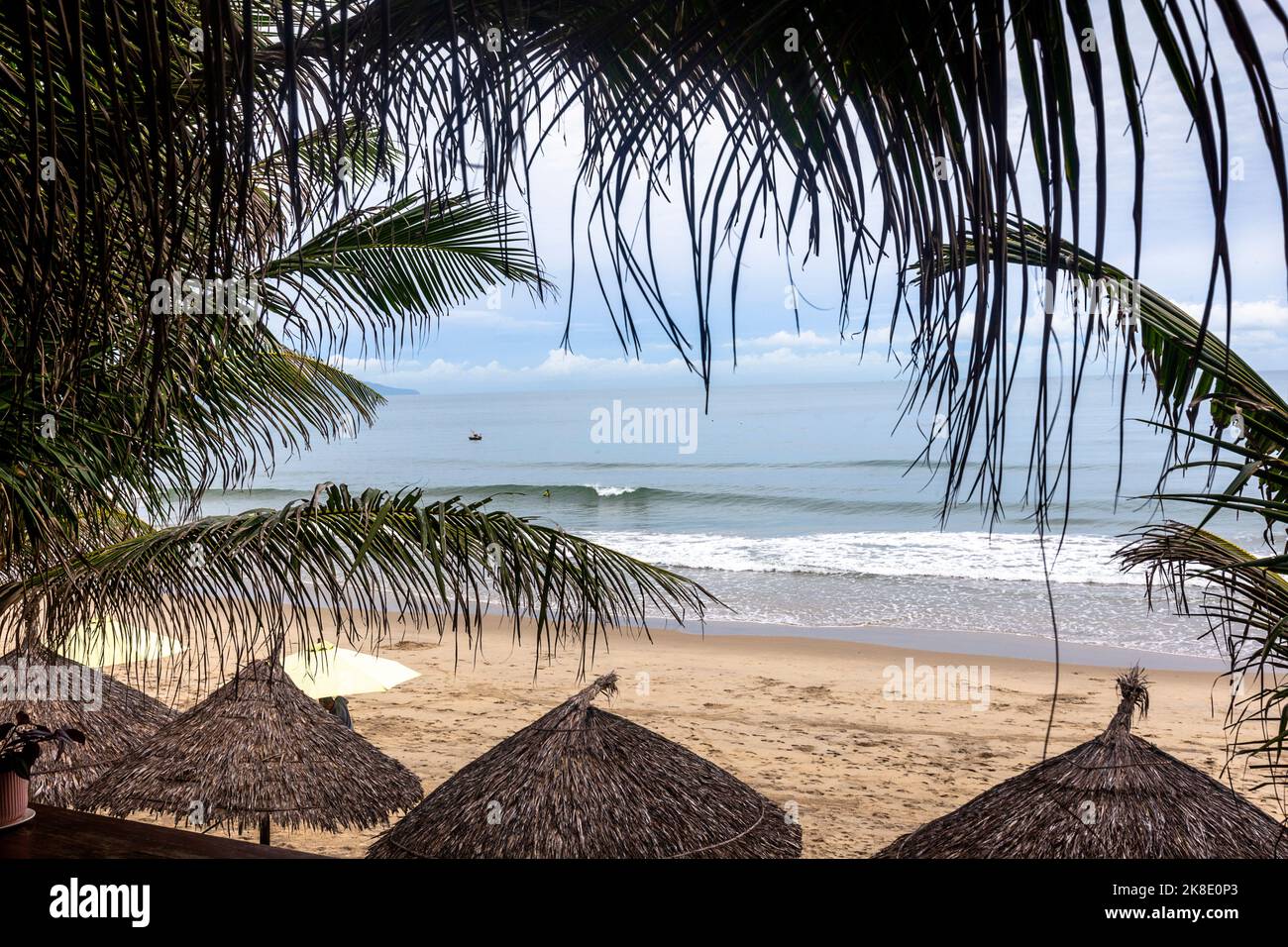 Ein erhöhter Blick auf das Meer mit Strandhütten und Fußabdrücken im Sand, die durch ein kleines Fenster mit Palmen blicken. Stockfoto