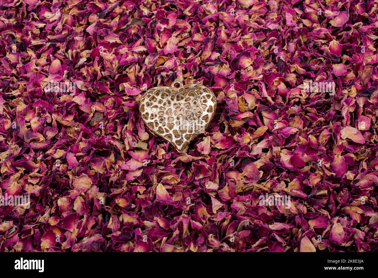 Goldene Farbe Herz auf trockenen Rosenblüten Hintergrund Stockfoto