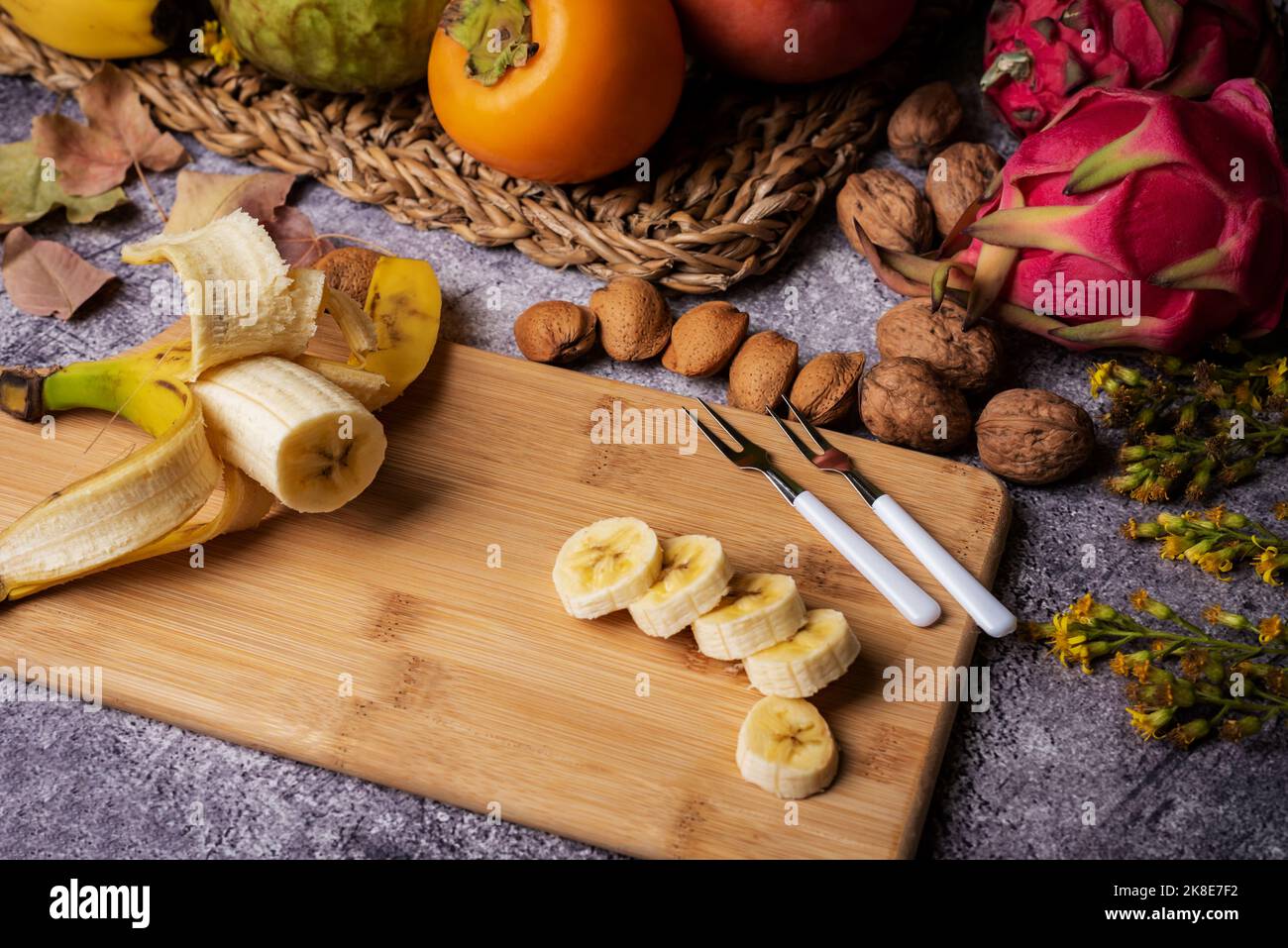 Banane kanarischen Ursprungs auf einem Holzbrett in Scheiben geschnitten, begleitet von tropischen Früchten wie Pitahaya, Kakimmon und Pudding Apple. Stockfoto