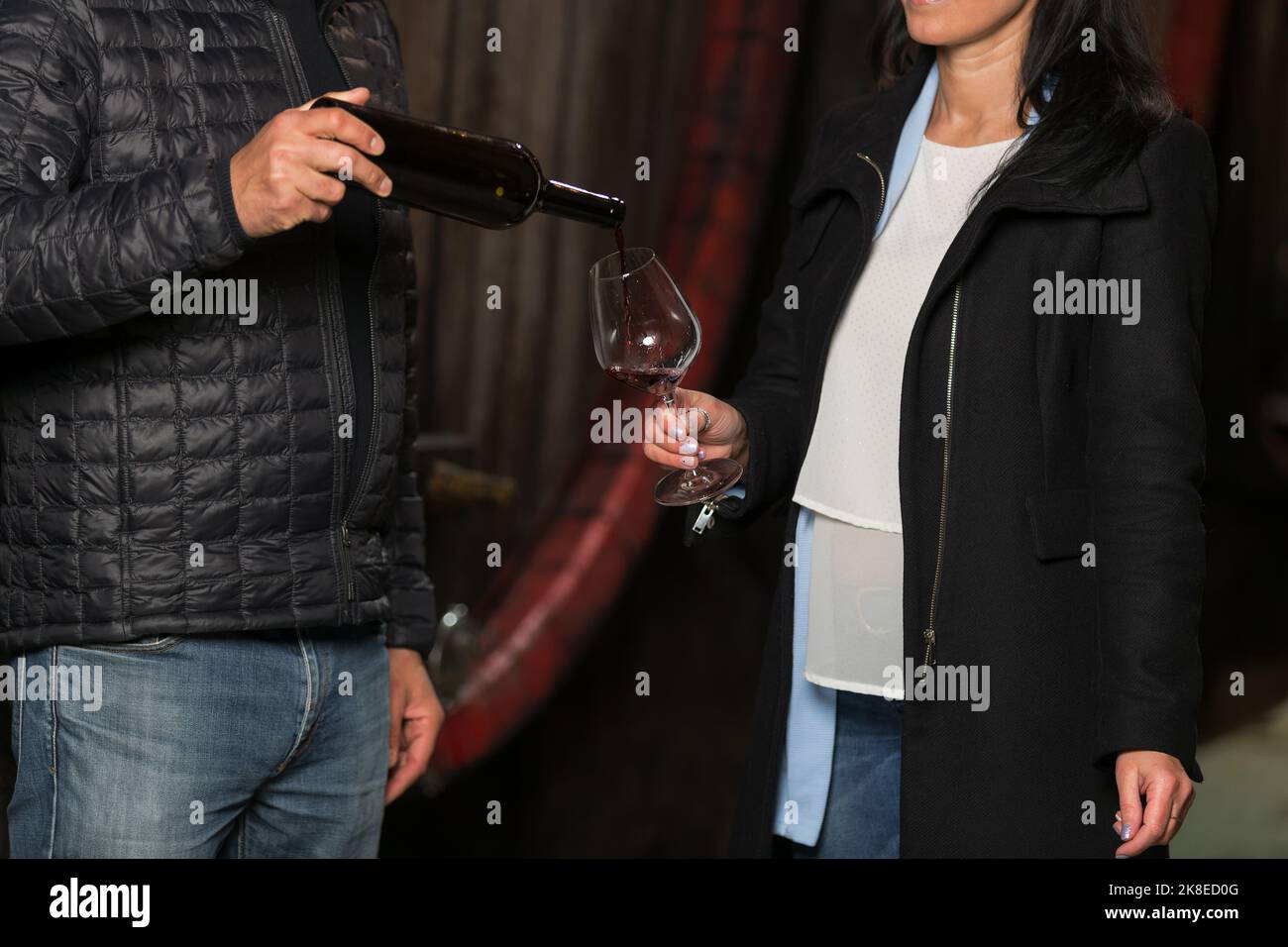 Kellermeister, oder Winzer gießt Rotwein für eine Frau, um ihn zu probieren und erklärt ihr Weinsorten Stockfoto