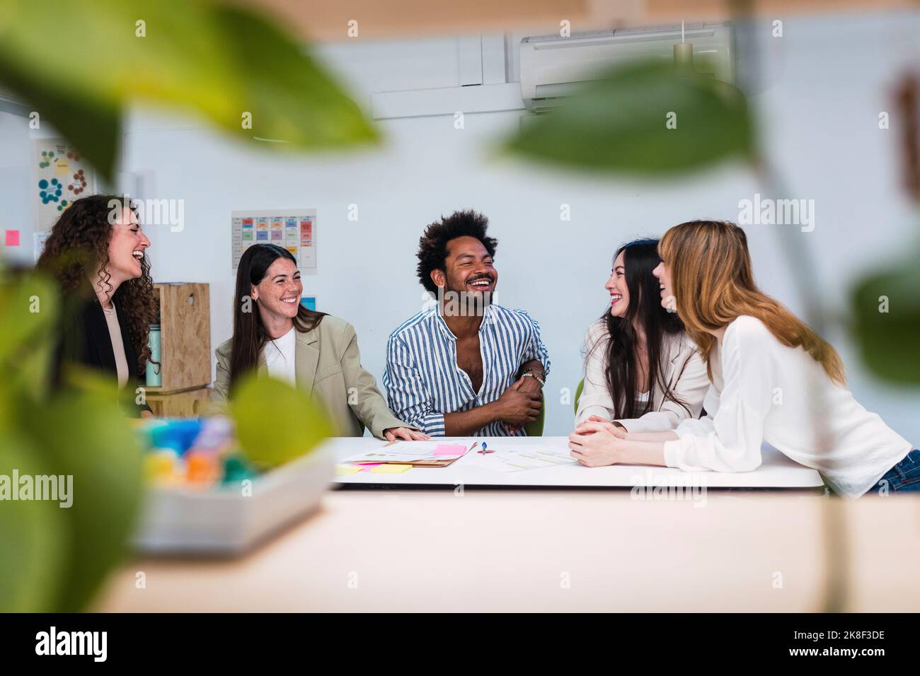 Glückliches Geschäftsteam, das am Tisch im Büro spricht Stockfoto