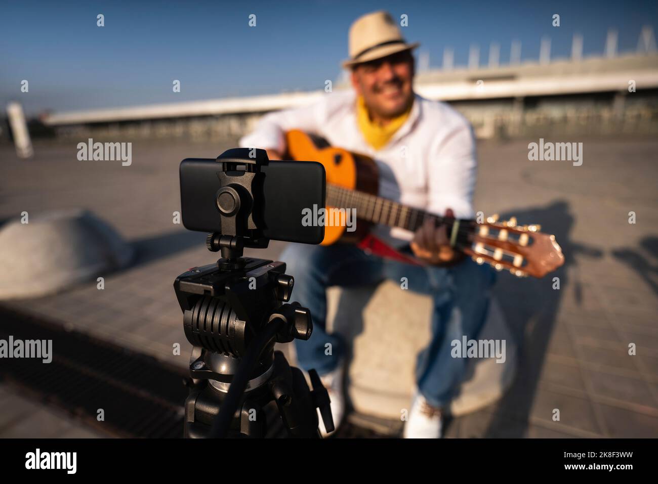 Straßenmusiker, der Gitarre spielt und über ein Mobiltelefon auf einem Stativ aufnimmt Stockfoto