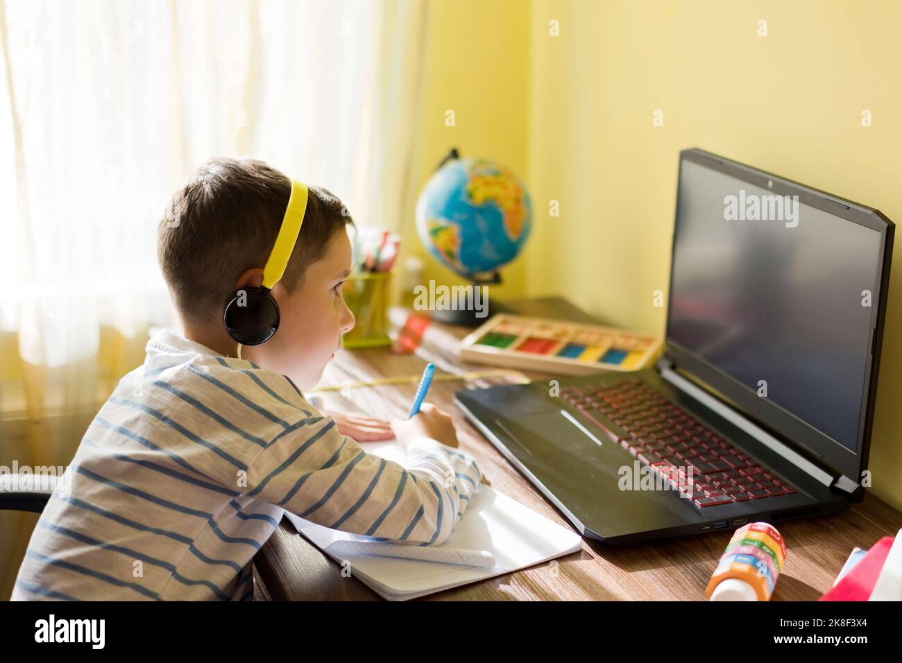 Junge, der Kopfhörer trägt und zu Hause einen Laptop benutzt Stockfoto