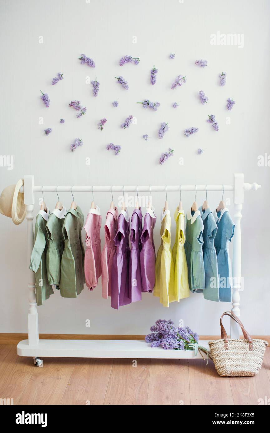 Mehrfarbige Kleider, die auf dem Regal vor der Wand mit Blumen hängen Stockfoto