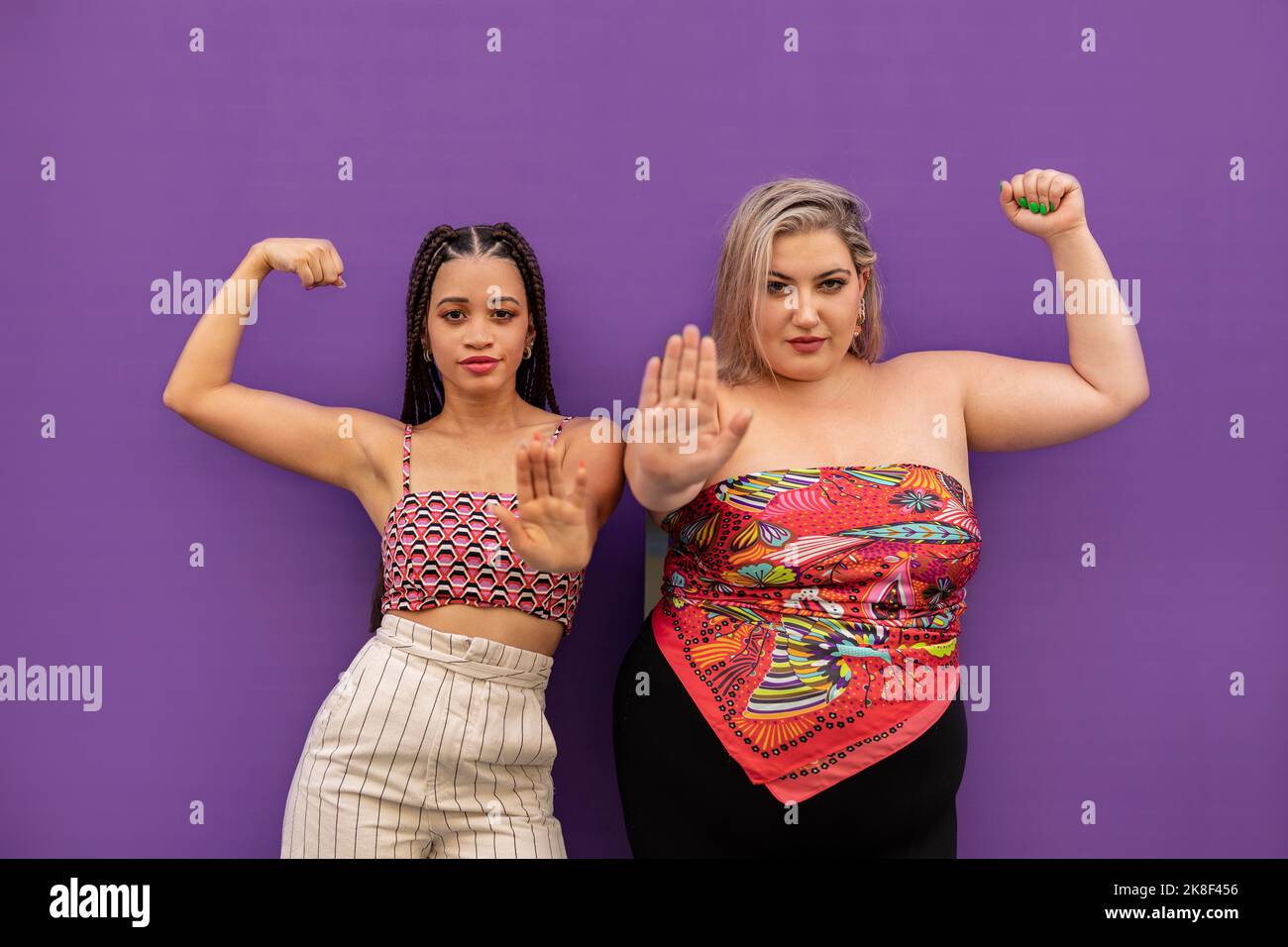 Junge Frauen biegen Muskeln und gestikulieren Stop-Zeichen vor der lila Wand Stockfoto