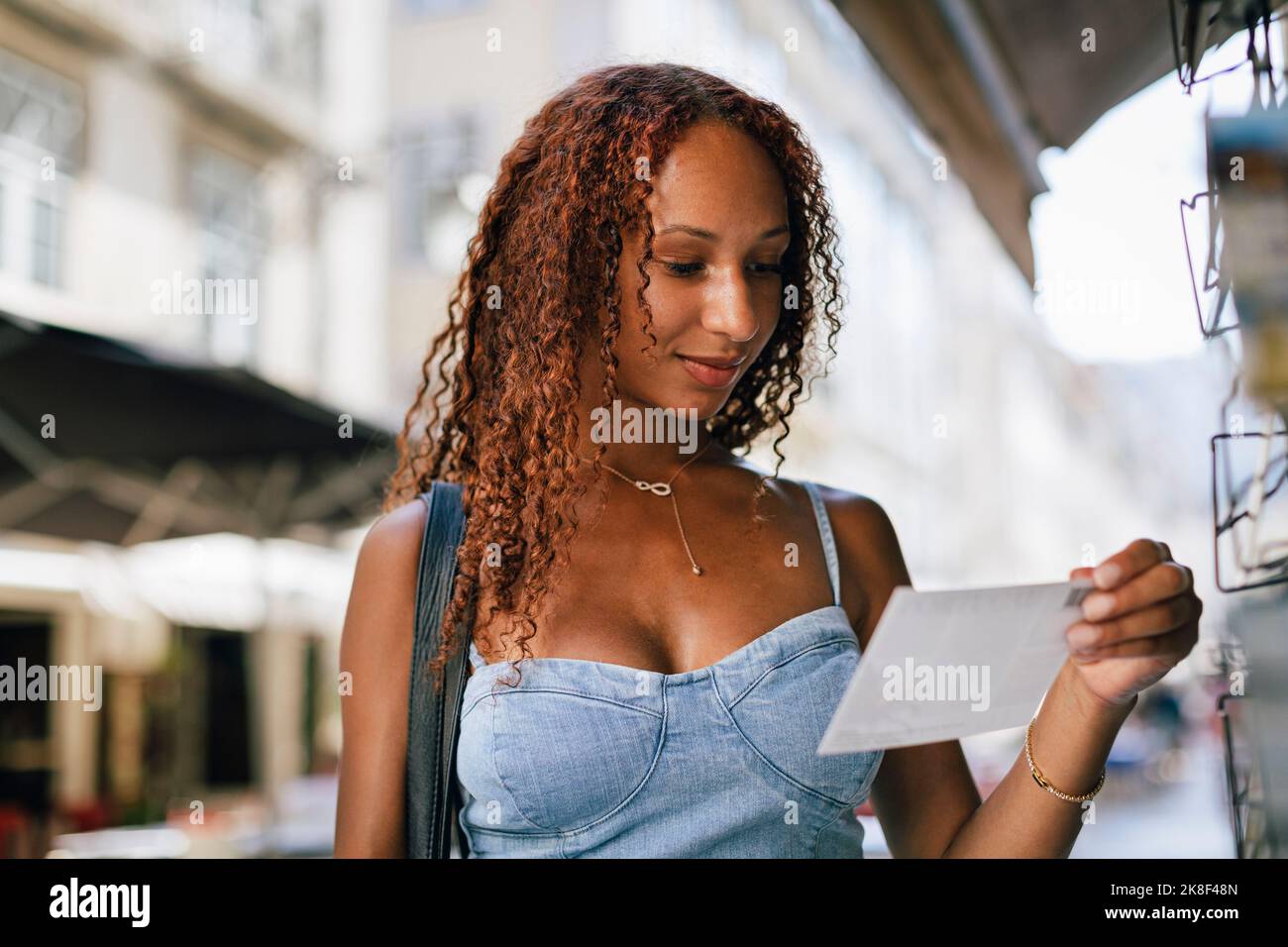 Lächelnde junge Frau mit lockigen Haaren, die auf eine Postkarte schaut Stockfoto