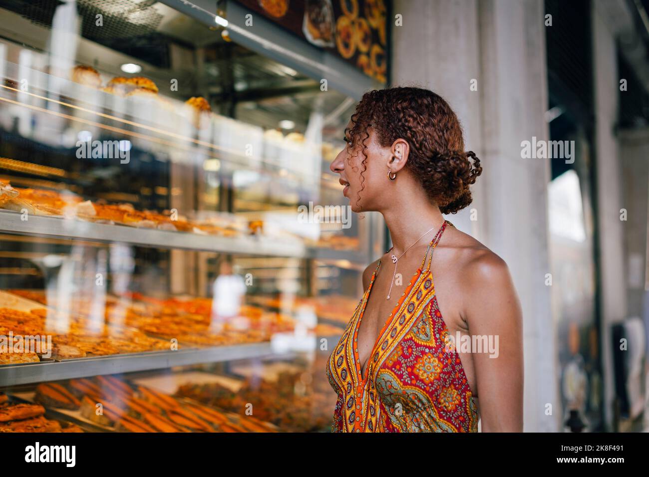 Junge Frau schaut durch das Fenster des Delikatessengeschäfts Stockfoto