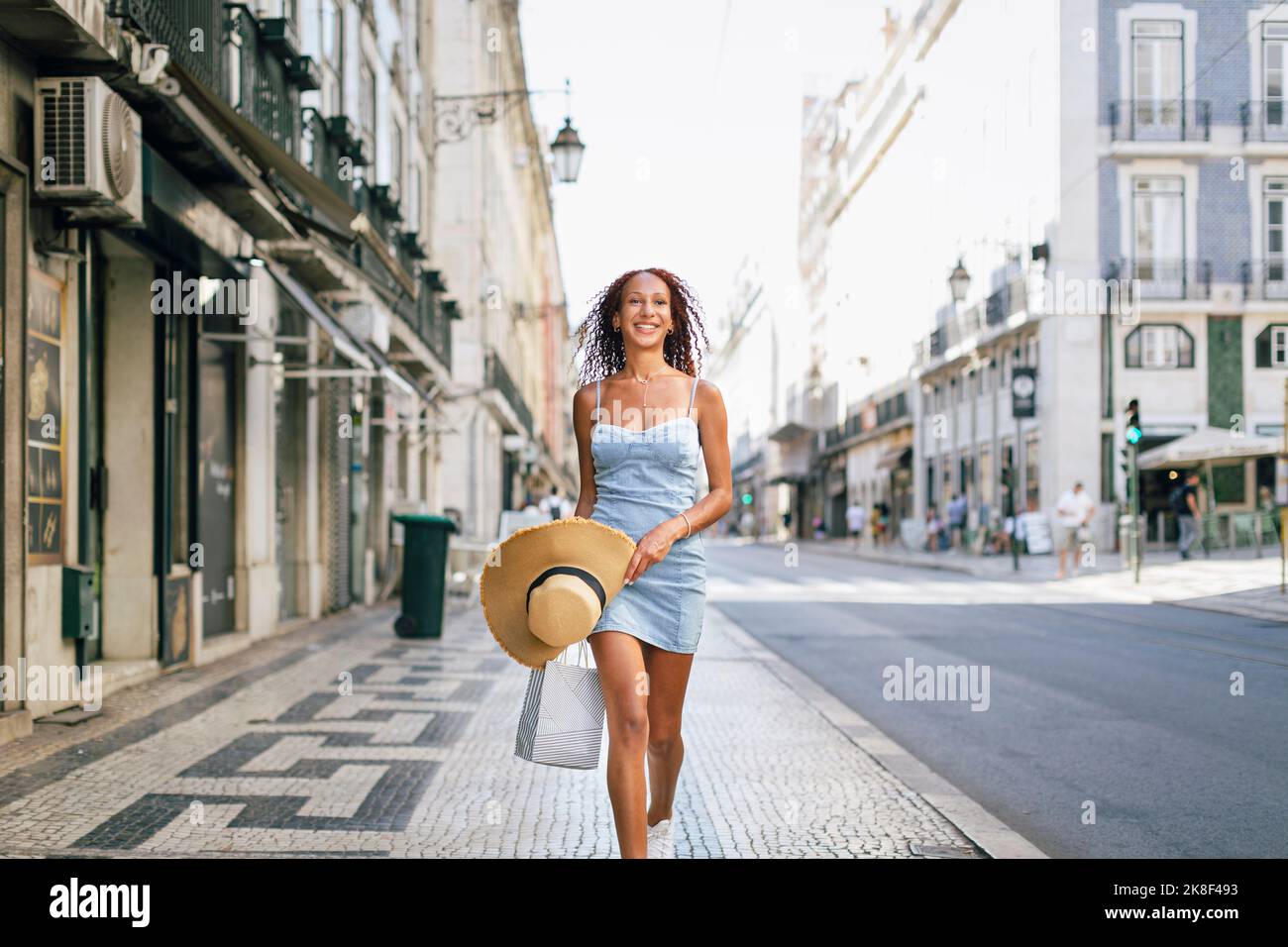 Glückliche junge Frau mit Hut und Einkaufstasche auf dem Fußweg Stockfoto